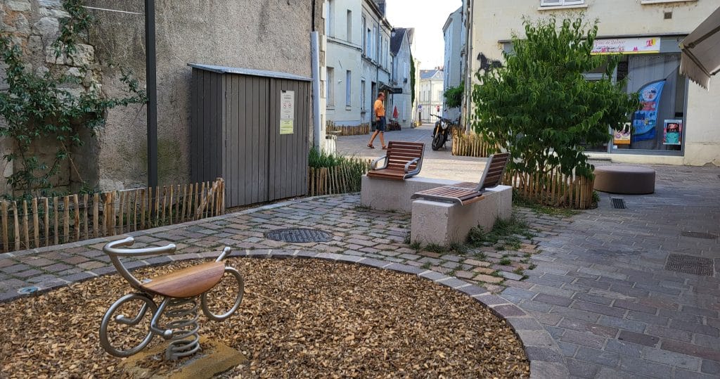 Petite aire de jeux urbaine avec bancs et pavés.
