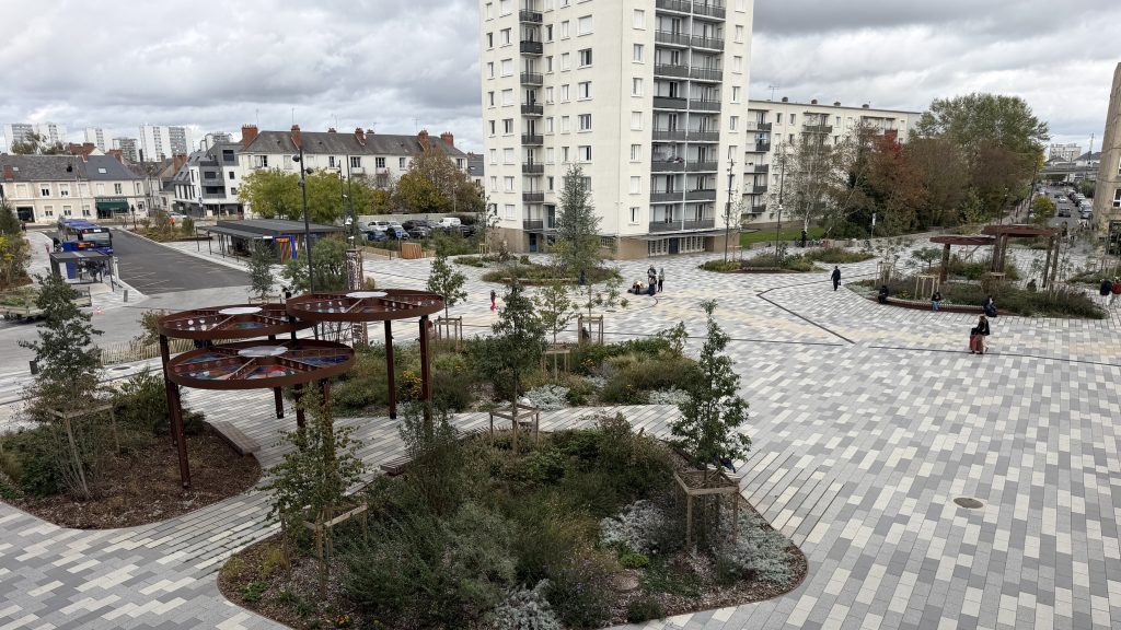 Place urbaine moderne avec pavés, végétation et immeubles résidentiels.